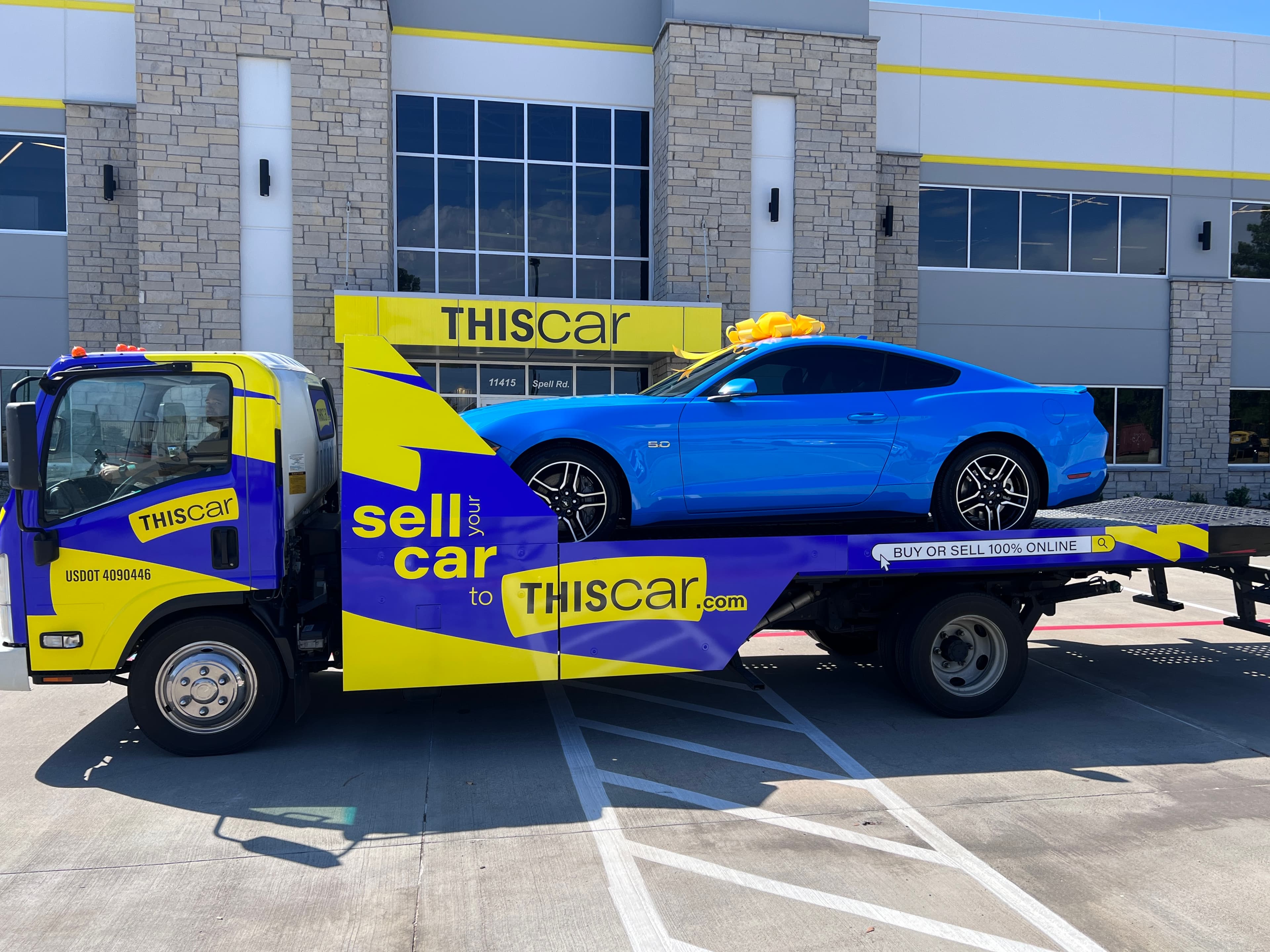 A THIScar hauler truck delivering a car in front of a THIScar location